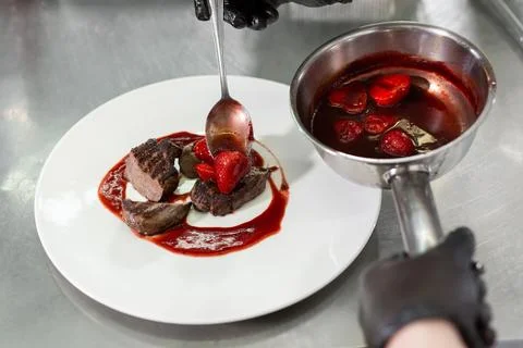 Chef decorates the meat with strawberries. Stock Photos