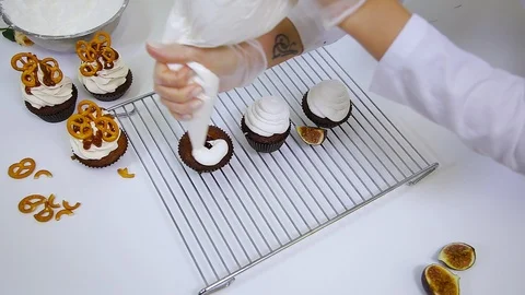 Chef is decorating brown cupcakes with white cream using pastry bag Stock-Footage 106614532