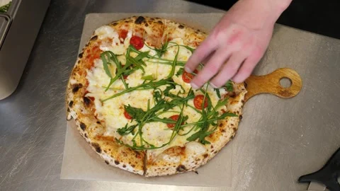 A chef decorating a freshly baked pizza with arugula in the pizzeria kitchen. Stock Footage 307392323