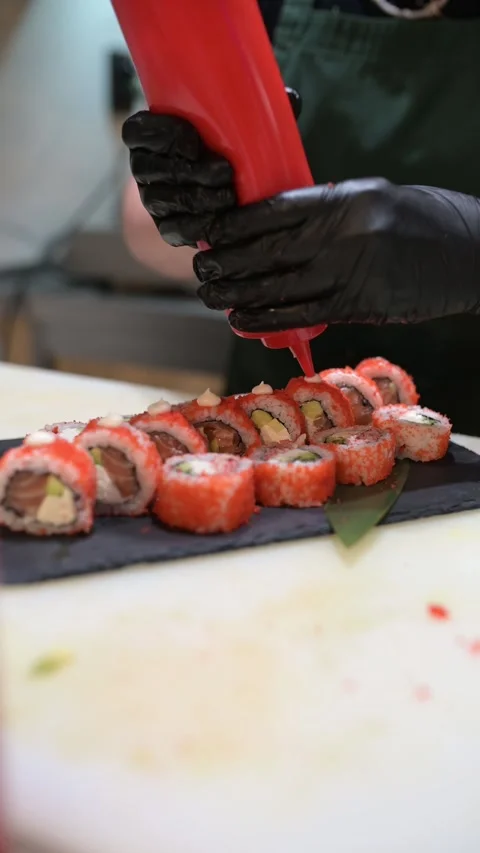 Chef decorating sushi rolls with sauce in a professional kitchen, adding final Stock Footage 314501755