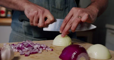 Chef dicing onions in home kitchen wearing blue apron Stock Footage 247786793
