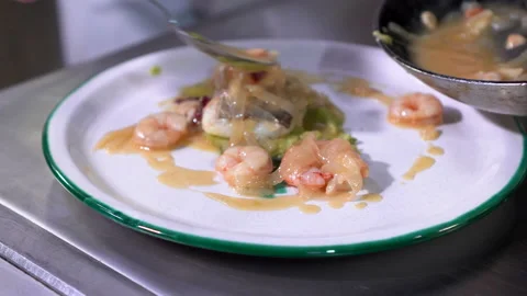 The chef distributes the sauce over the delicious dish of cod with prawns. In Stock Footage 143793918