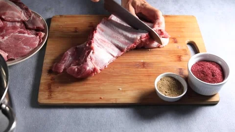 The chef divides pork ribs into pieces on a wooden board with a knife Stock Footage 157477519