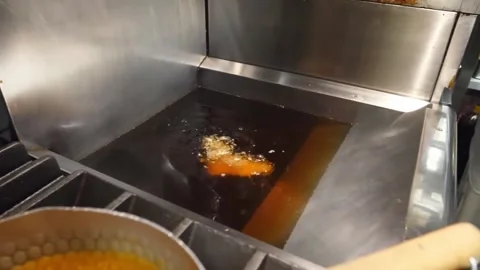 Chef dropping battered fish into commercial deep fryer Vídeos de archivo 347688024