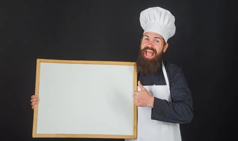 Chef with empty menu board. Smiling cook or baker shows thumb up. Advertising Stock Photos