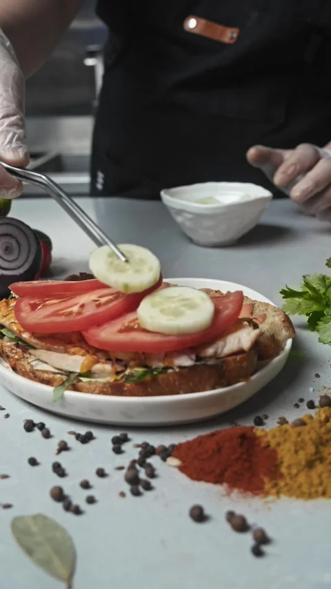 Chef of an expensive restaurant in the kitchen adds cucumbers to a sandwich with Stock Footage 292155972