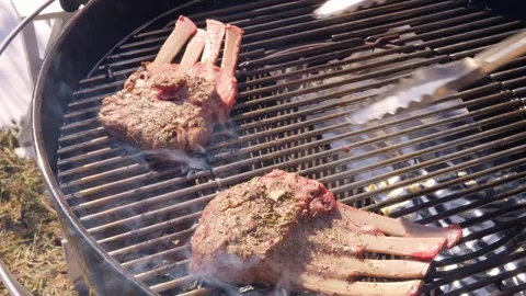 Chef expertly flips lamb ribs on grill to ensure even cooking. Watch as meat Stock-Footage 273759239