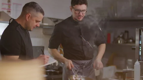 Chef Explaining Recipe to Apprentice Taking Notes in Restaurant Kitchen Stock-Footage 330062457
