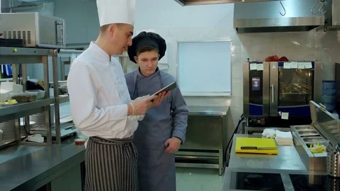 Chef explaining something to cook trainee in hat using digital tablet Vídeos de archivo 72323913