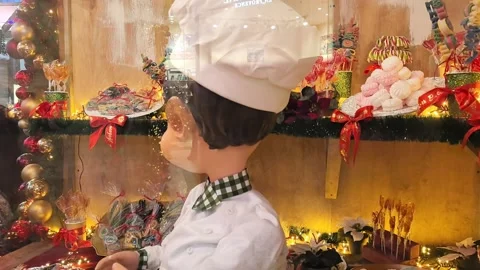 Chef figure stands in bakery window with holiday decorations and treats on displ Stock Footage 325174360