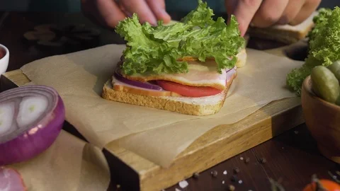 Chef finalizes the sandwich with ham and salad on the wooden board in the beam Stock Footage 113264848