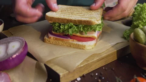 Chef finalizes the sandwich with ham and salad on the wooden board Stock Footage 143777972