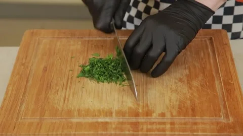A chef finely chopping fresh dill and parsley on a cutting board using a knife Stock Footage 340553125