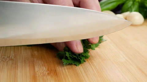 A chef is finely chopping fresh green parsley on a wooden cutting board.  Vídeos de archivo 341476806