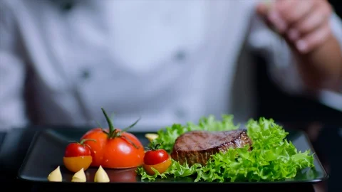Chef is finishing the delicious beef dish with greens. Chef is out of focus on Stock Footage 92519736