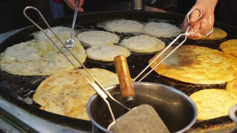 Chef flipping Cong You Bing scallion pancakes on griddle at street market Stock Footage 336442189