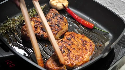 Chef flips a delicious steak with cooking tongs Stock Footage 333631092