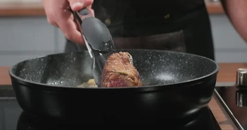 Chef flips juicy steak roasting with rosemary and garlic on a frying pan on Stock Footage 261743572