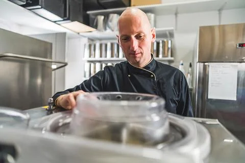 Chef focused on work standing over ice cream maker in kitchen with stainless Stock Photos