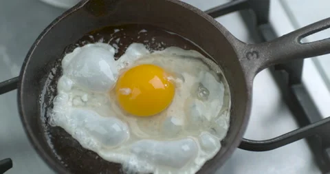 A chef fries an egg, sunny side up, in a small frying pan over industrial gas bu Stock Footage 199459682
