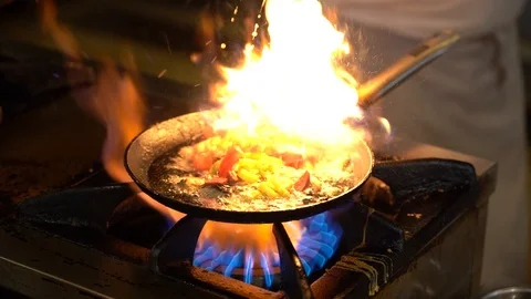 Vegetables fry on a large frying pan on fire. Cooking at the festival. Girl  chef pouring vegetables into disposable utensils. Stock Photo