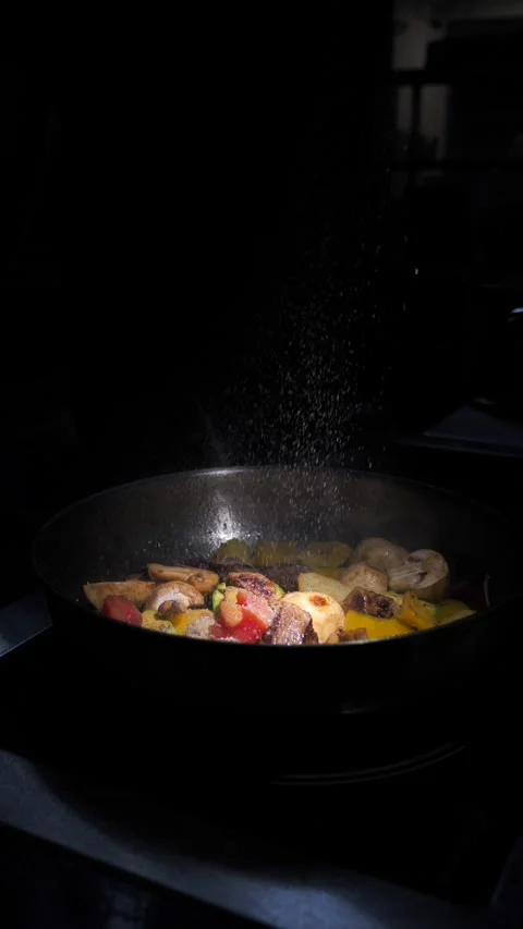 Chef frying vegetables with meat, sprinkling them with spices in a frying pan. Stock Footage 309463560