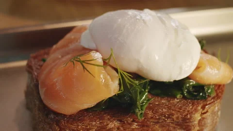 The chef gently puts poached egg on a brioche sandwich with spinach and salmon 스톡 동영상 150841536