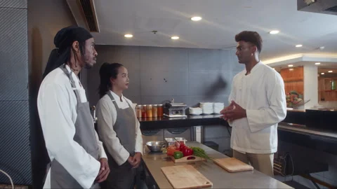 Chef Giving Instructions about Menu to Team Cooking Dishes at Restaurant Kitchen Stock Footage 257751232