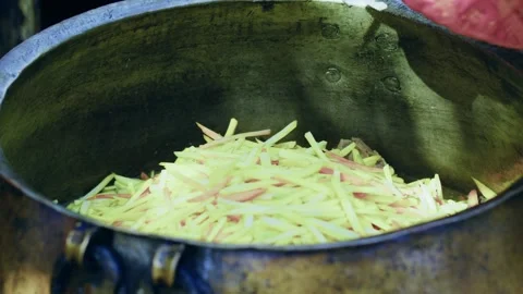 Chef in gloves adding sliced carrots to huge kazan pot while cooking Uzbek plov, Stock Footage 346702416