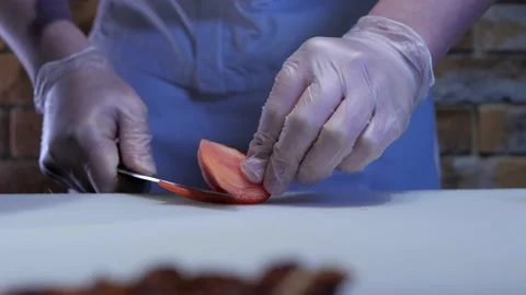 Chef in gloves and apron is cutting tomato, preparing ingridients for the dish. Stock Footage 135175411