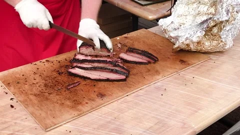Chef in gloves and an apron with a sharp knife cuts the meat baked on the grill 스톡 동영상 249506331