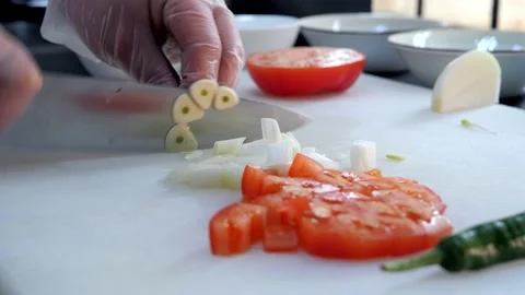Chef in gloves cuts garlic, tomatoes and jalapenos on the white cutting board. Stock Footage 132828270