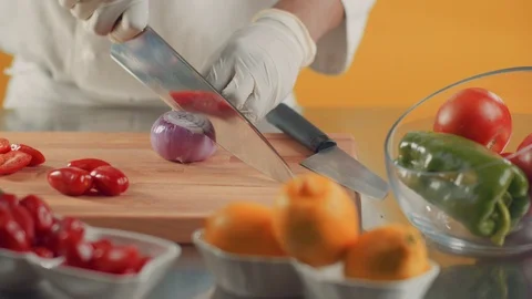 Chef in gloves is cutting onion with sharp knife on wooden board, vegetables on Stock Footage 105284878