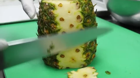 Chef in gloves dicing a ripe pineapple on a green cutting board in a professiona 스톡 동영상 332811413