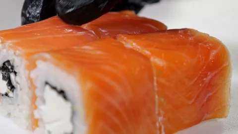 A chef in gloves prepares sushi, he slices sushi with salmon with a large knife. Stock Footage 321813906