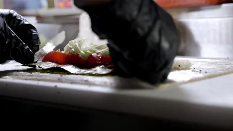 A chef in gloves prepares sushi rolls on a bamboo mat in a professional kitchen. Stock Footage 323363969