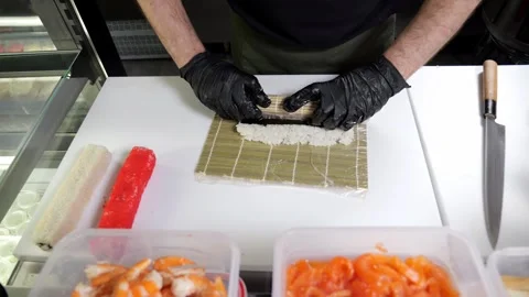 A chef in gloves prepares sushi rolls on a bamboo mat in a professional kitchen. Stock Footage 325181704
