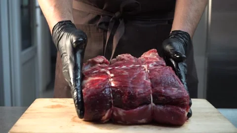 A chef with gloves puts a raw piece of meat on a cutting board Stock Footage 144873388