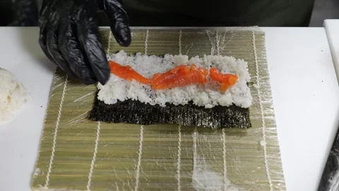A chef in gloves puts sliced salmon slices on rolls in the restaurants kitchen. Stock Footage 327643922