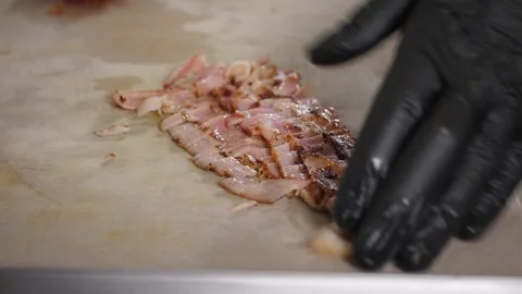 A chef in gloves slicing fried bacon with a knife on a cutting board. Stock Footage 344038636