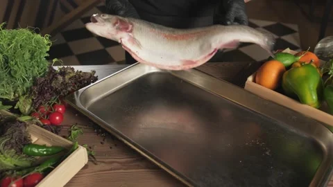 Chef in gloves throwing fish on a tray standing on a table among herbs and Stock Footage 315283466