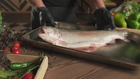 Chef in gloves throwing fish on a tray standing on a table among herbs and Stock Footage 339877912
