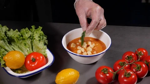 A chef in gloves throws slices of croutons and puts a leaf of dill in a soup. Stock Footage 127959736