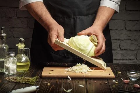 The chef grates fresh cabbage with a hand grater to prepare a vegetable dis.. Stock Photos