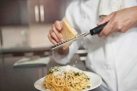 Chef Grating Cheese Onto Pasta In Kitchen Stock Photos