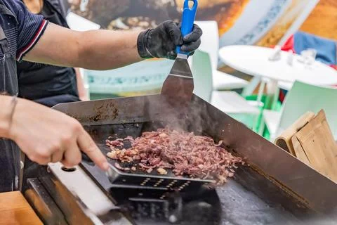 Chef grilling meat on flat top griddle in busy outdoor kitchen setting Stock Photos