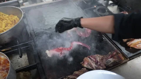 Chef grilling octopus tentacles on a restaurant plancha grill 스톡 동영상 323792451