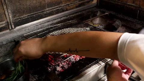 Chef Grilling Whole Fish Over Charcoal With Fresh Herbs in Rustic Kitchen Stock Footage 337987952