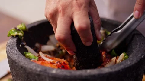 Chef grinds and prepares fresh roasted mexican salsa in a stone molcajete bowl Stock Footage 288038789