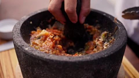 Chef grinds and prepares fresh roasted mexican salsa in a stone molcajete bowl Stock Footage 288038814
